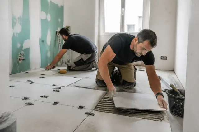 Deux artisans posent du carrelage pour artisan-en-1-clic.fr dans une salle en rénovation
