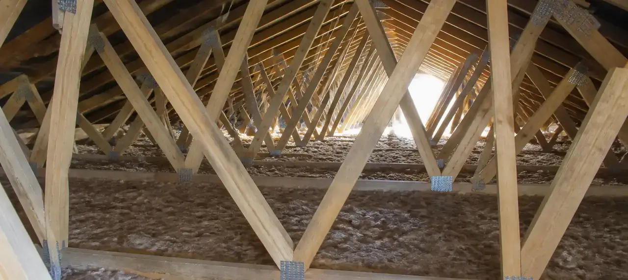 Fermettes en bois assemblées par connecteurs métalliques, alignées dans un comble perdu