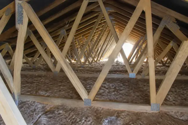 Fermettes en bois assemblées par connecteurs métalliques, alignées dans un comble perdu