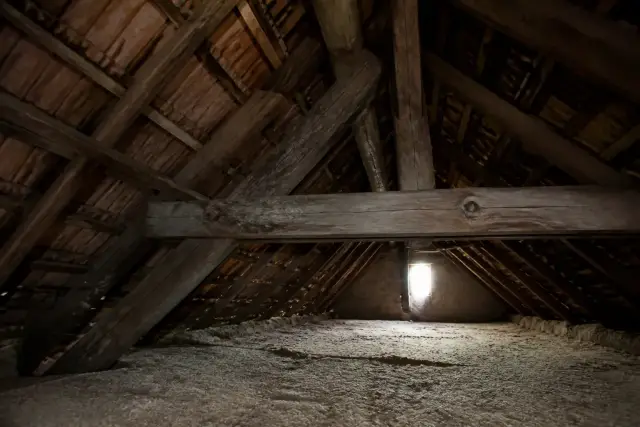 Combles d’une maison ancienne avec chevrons et pannes en bois, lampe de chantier posée sur un plancher