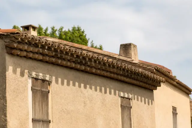 Avancée de toit en tuiles canal sur une façade enduite, avec une génoise à plusieurs rangs