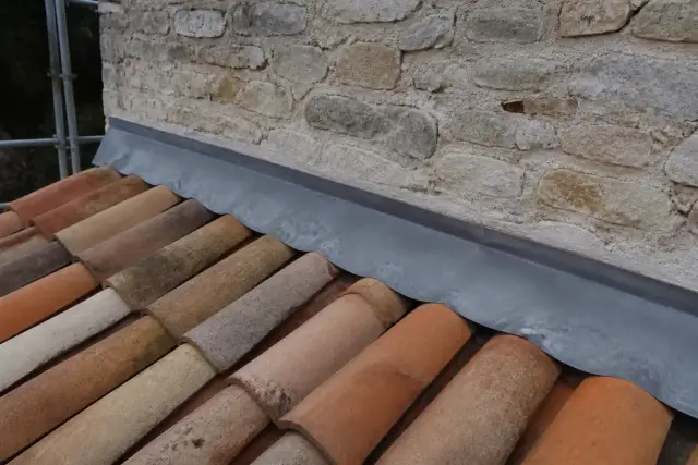 Bande de solin en zinc engravée dans un mur de pierre, au-dessus d’un rang de tuiles en terre cuite
