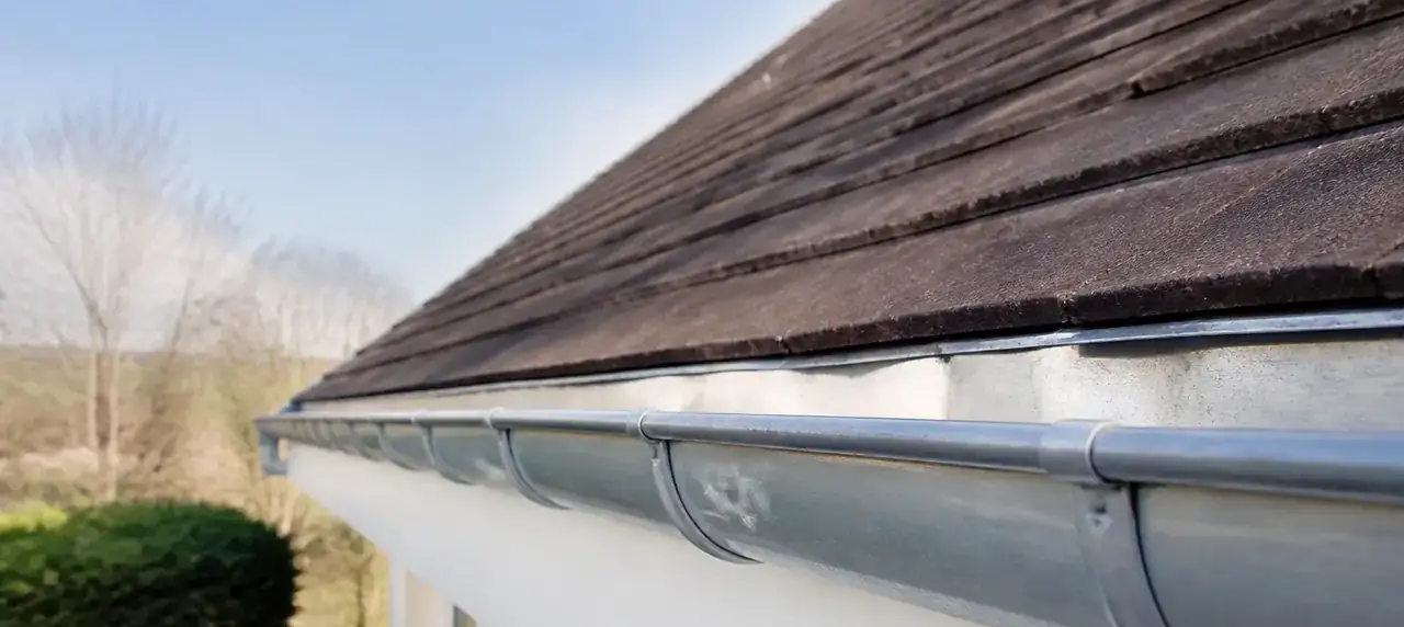 Toit de tuiles plates propres sous un ciel clair, avec une gouttière en zinc nettoyée au premier plan