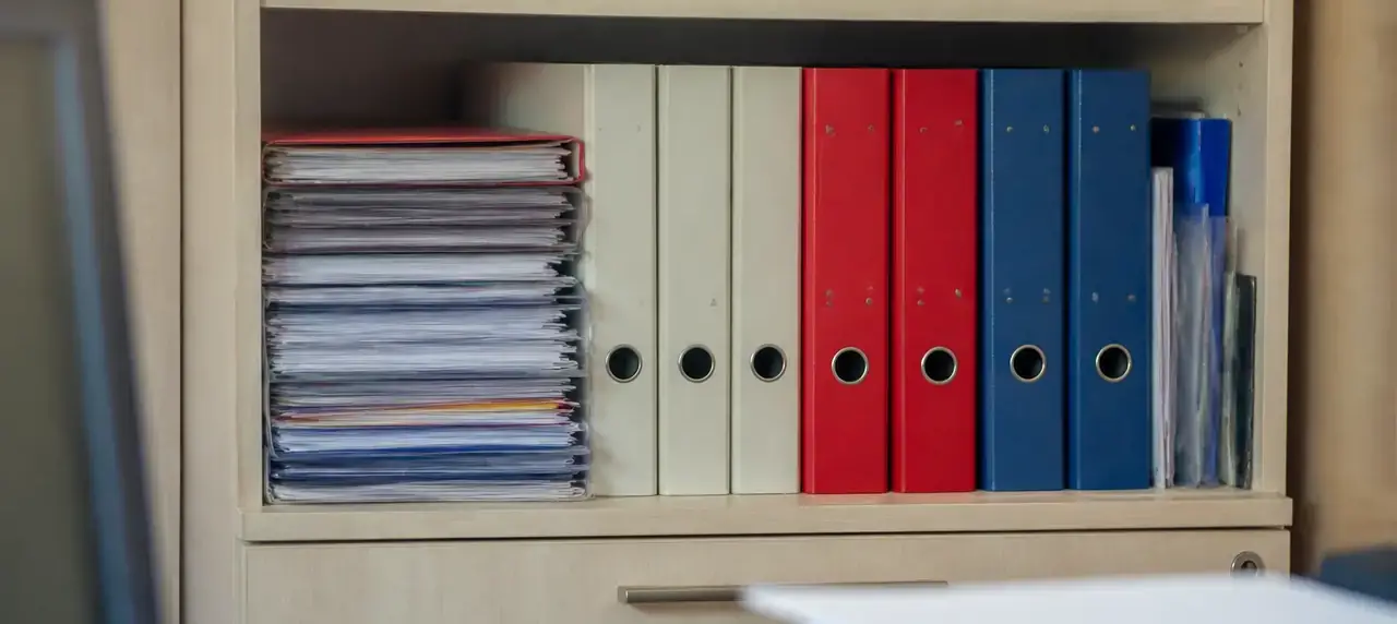 Pile de dossiers et de classeurs rangés sur une étagère de bureau, sous une lumière douce