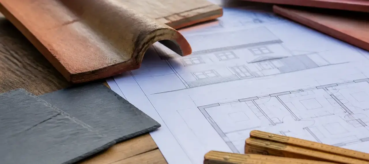 Plans de maison posés sur une table de bois avec des échantillons de tuile et d’ardoise et un mètre pliant