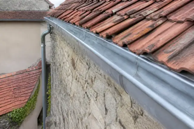 Chéneau en zinc posé en tête d’un mur de pierre séparant deux jardins, descente d’eau côté maison