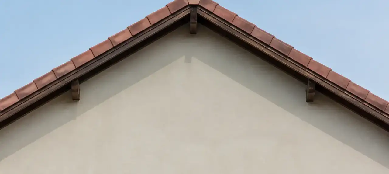 Pignon de maison à deux pans vu de face, versants nettement inclinés sous un ciel clair