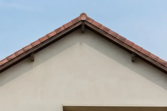 Pignon de maison à deux pans vu de face, versants nettement inclinés sous un ciel clair