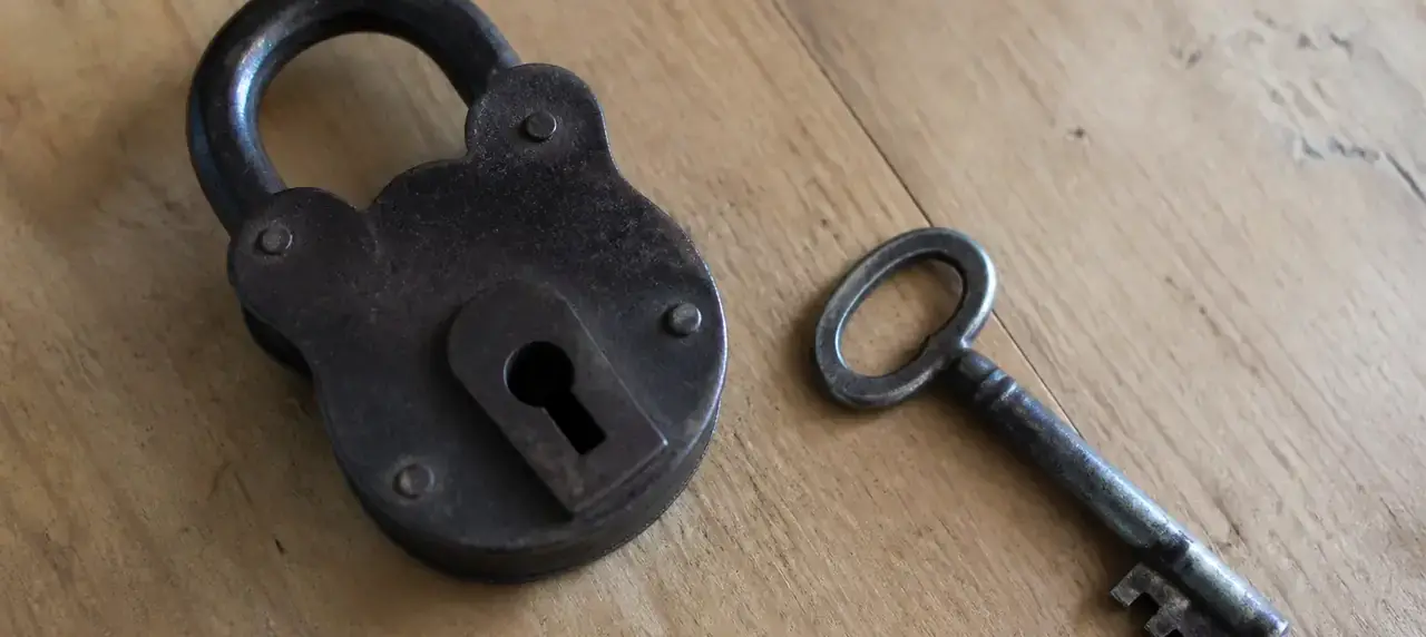 Cadenas ancien posé sur une table de bois clair à côté d’une clé, lumière naturelle